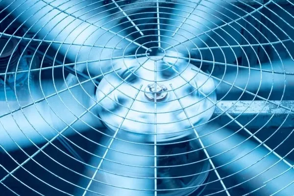 Close-up of AC condenser fan grille with spinning metal blades and motor housing visible through protective grid.