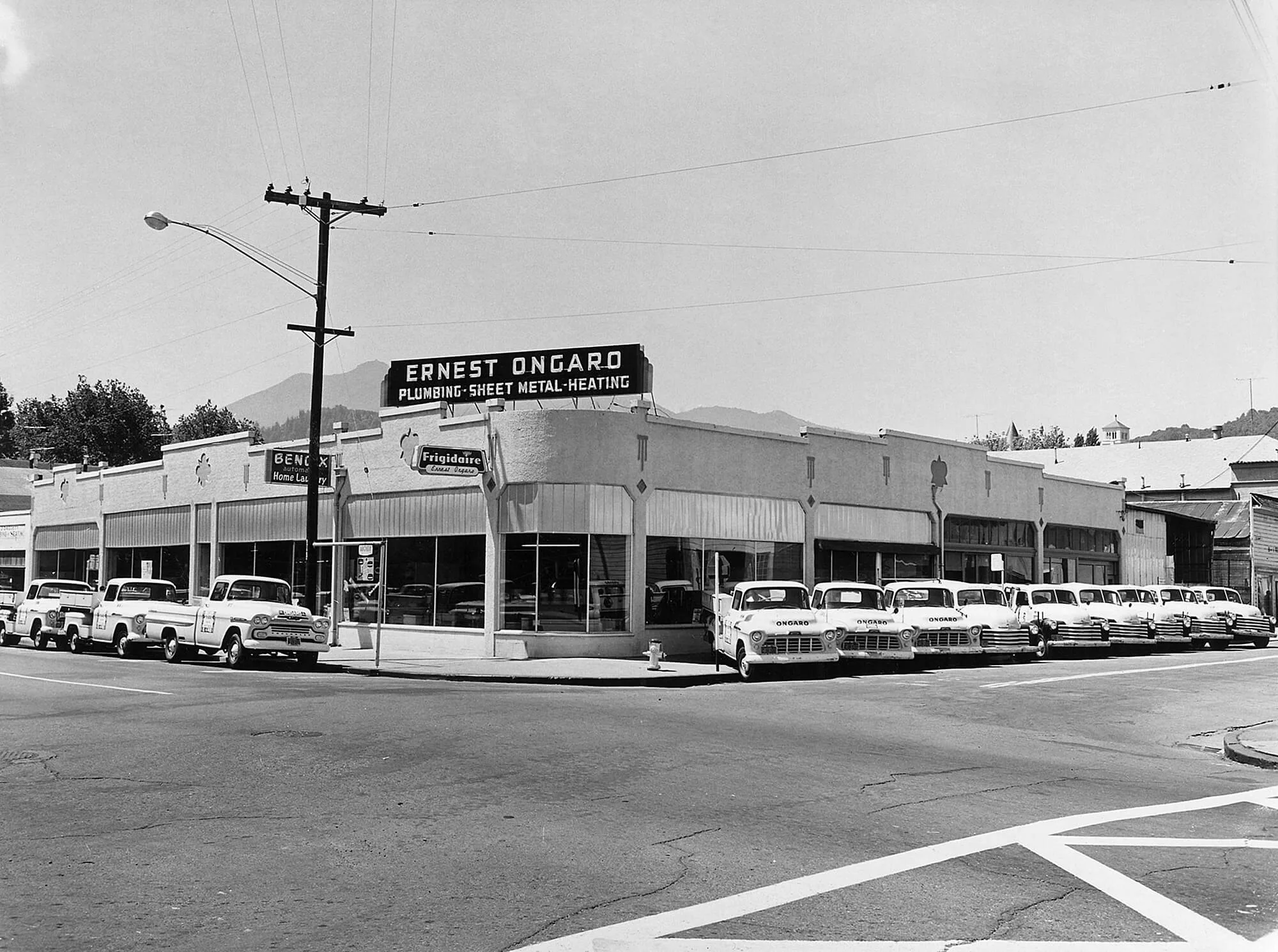 Ernest Ongaro's historic storefront with vintage cars parked outside, mid-20th century black and white photograph.