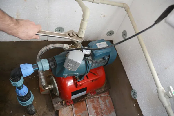 Technician's hand adjusting red and blue water pump system with PVC piping in basement installation