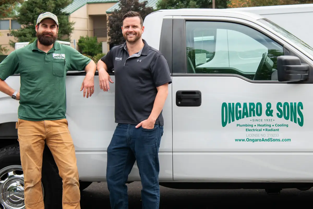 Ejay and Don Ongaro & Sons team members stand beside a white service van at the company shop, smiling at the camera.