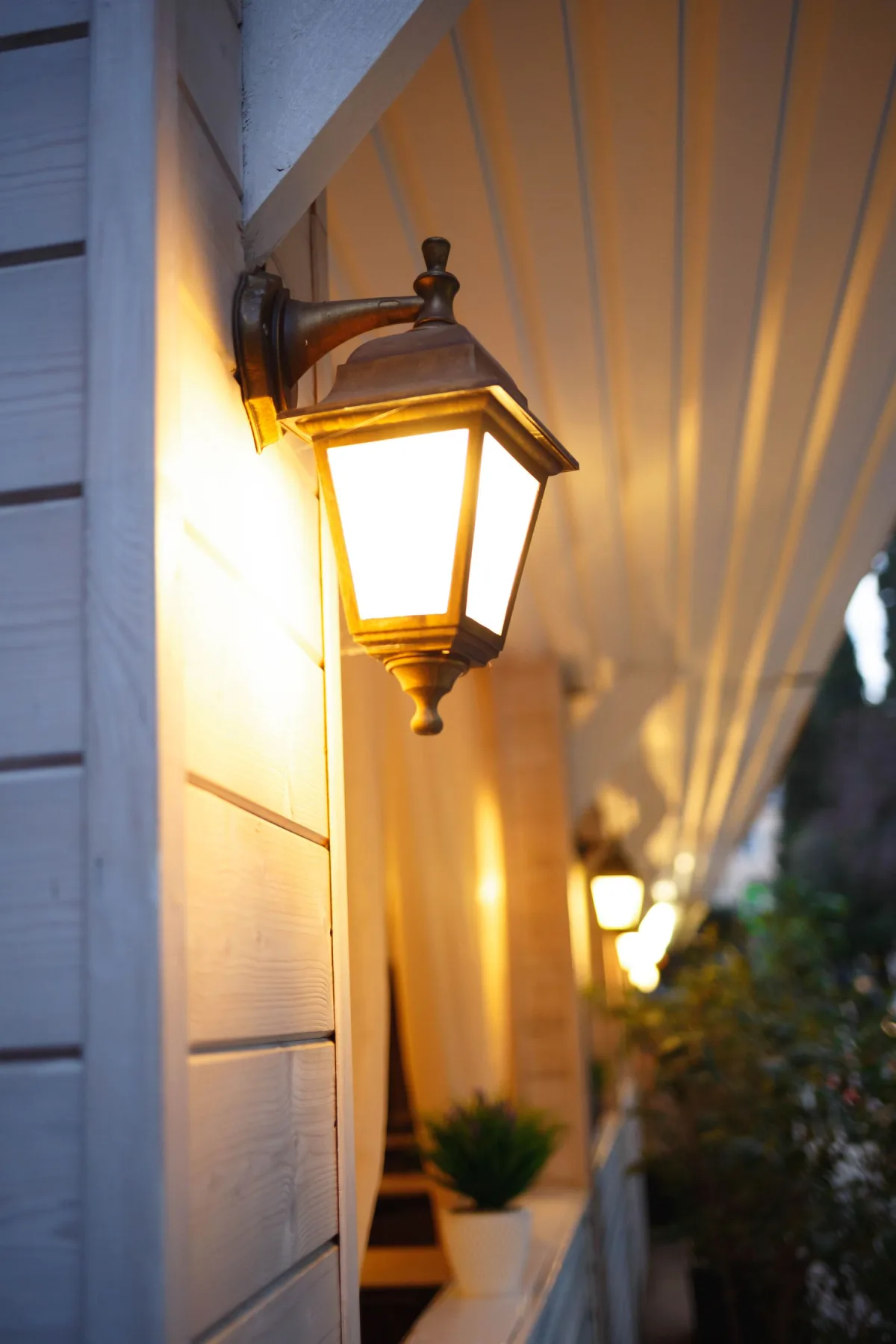 Warm-lit coach lantern mounted on the exterior siding of a home at dusk