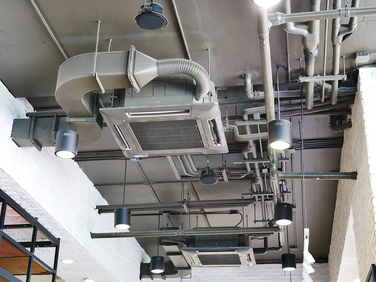Commercial HVAC system with ductwork, exhaust hood, and multiple ceiling-mounted components in industrial space.