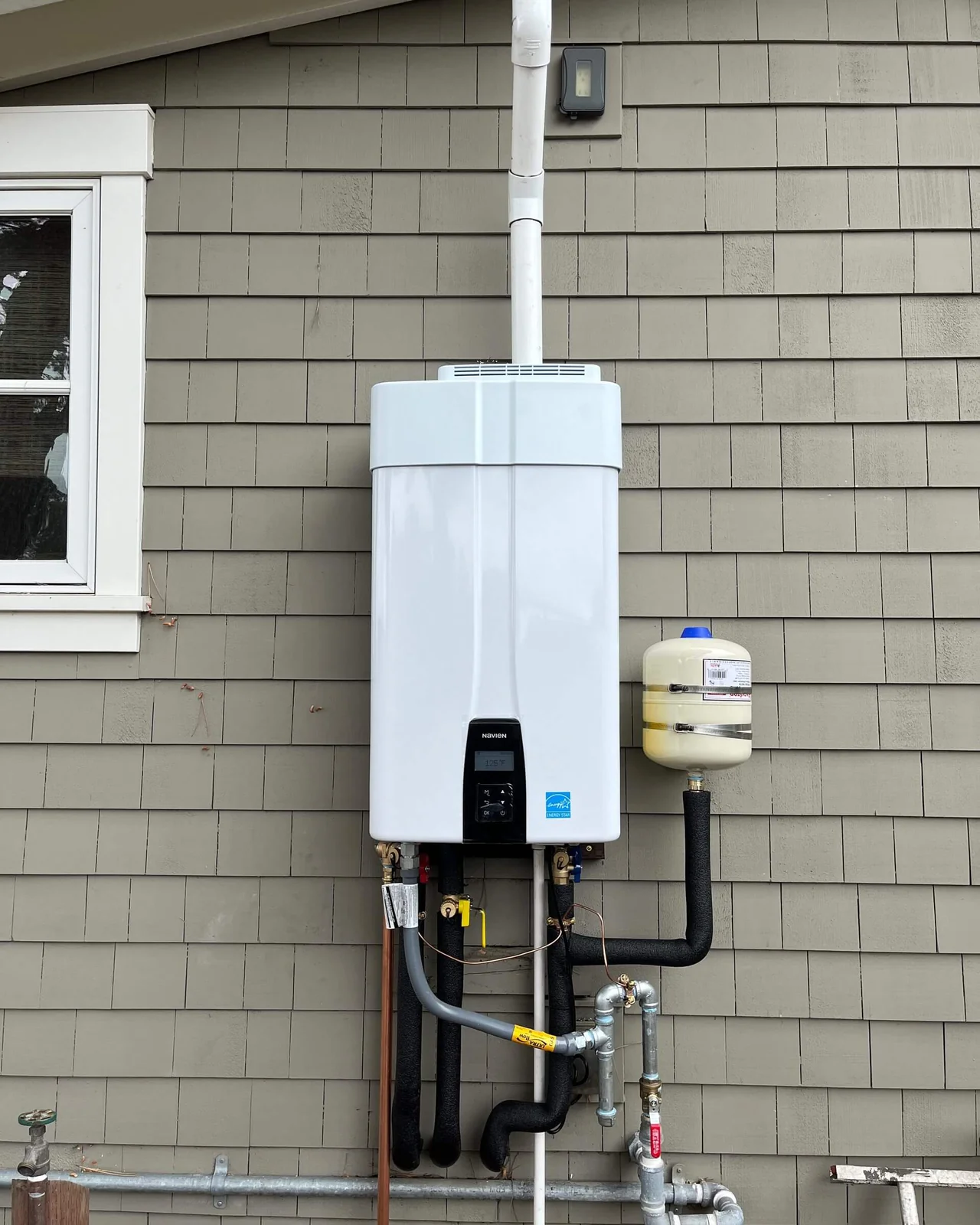 A Navien tankless water heater mounted on an exterior wall