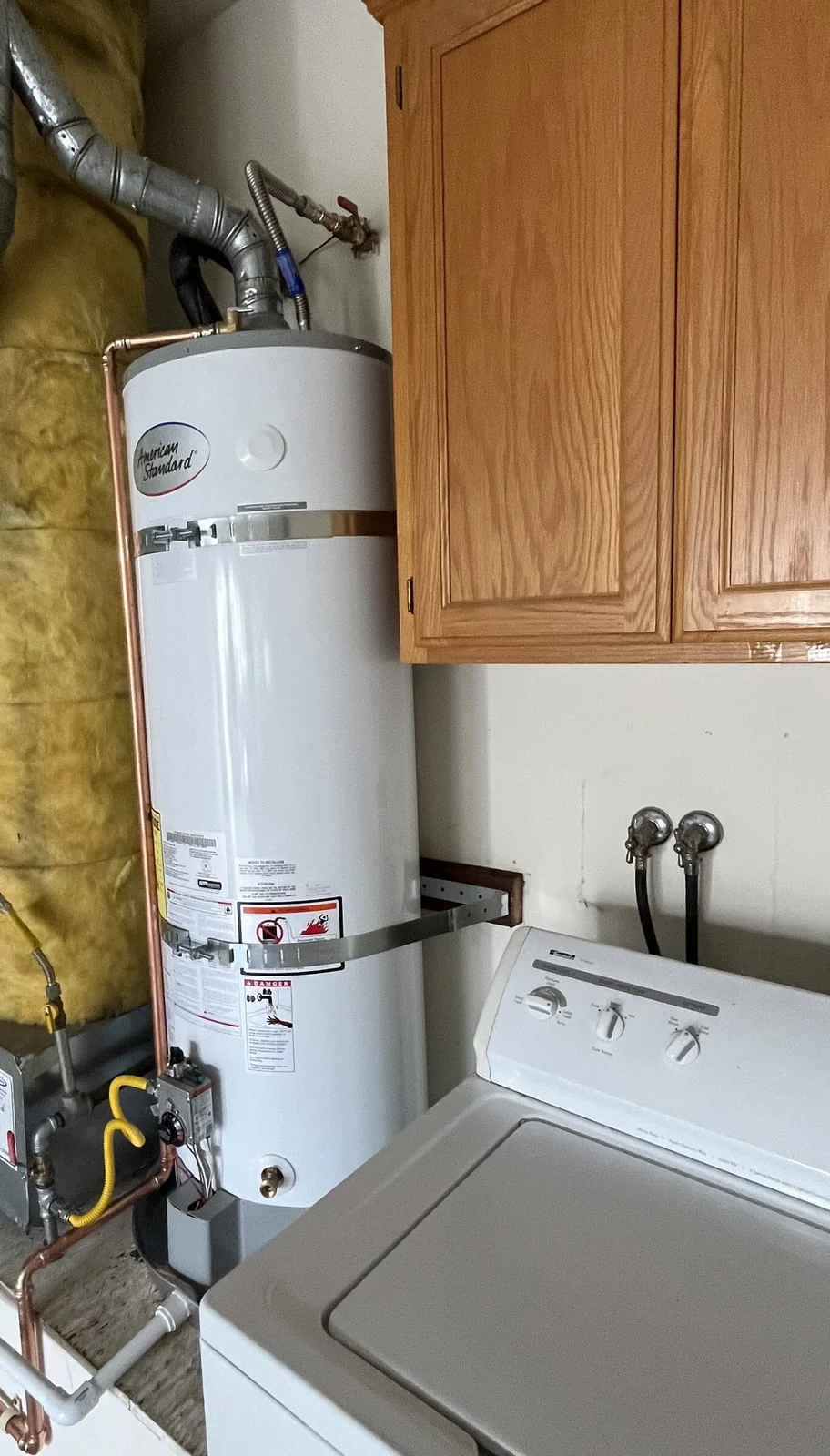 A strapped gas water heater beside the laundry hookups in a garage utility space