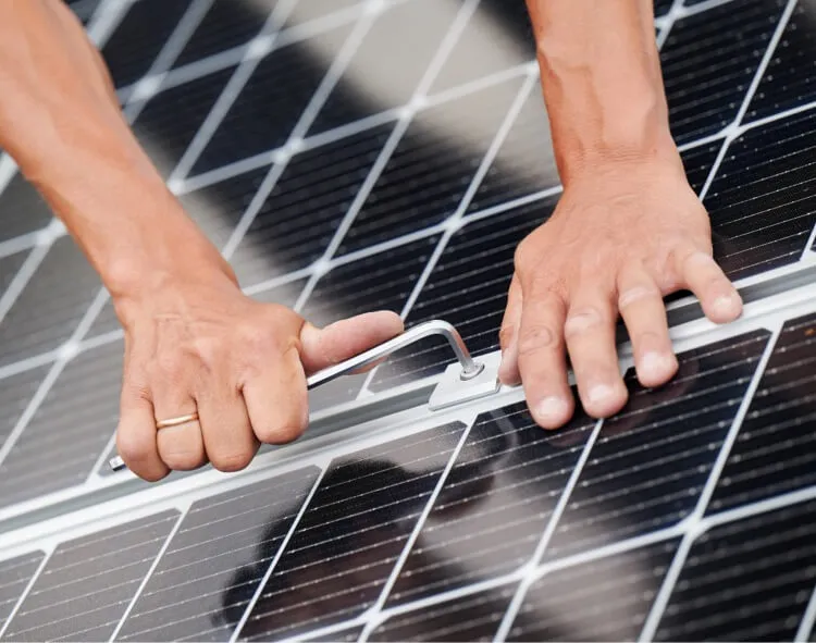 Technician's hands installing or adjusting a solar panel with white grid lines visible on the dark panel surface.